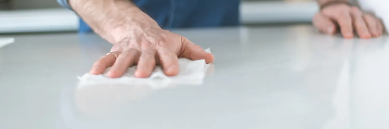 Eine Person wischt mit einem weißen weichen Tuch über eine Oberfläche mit dem Fokus auf Putzen