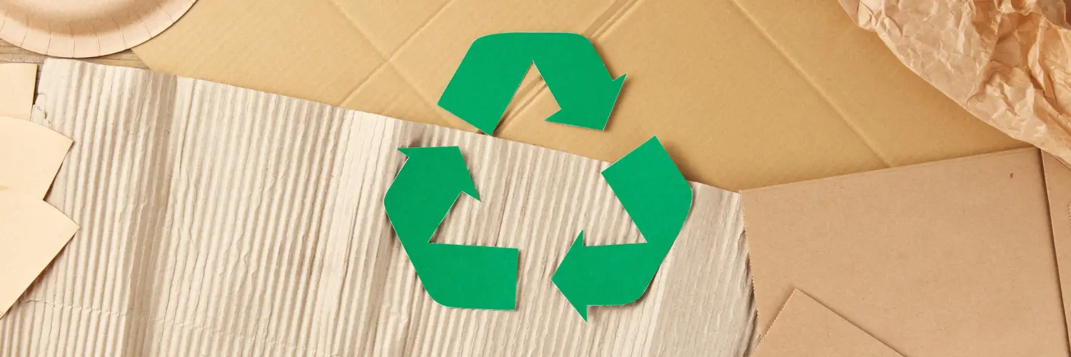 Grünes Recyclingsymbol auf Karton umgeben von Papierfetzen
