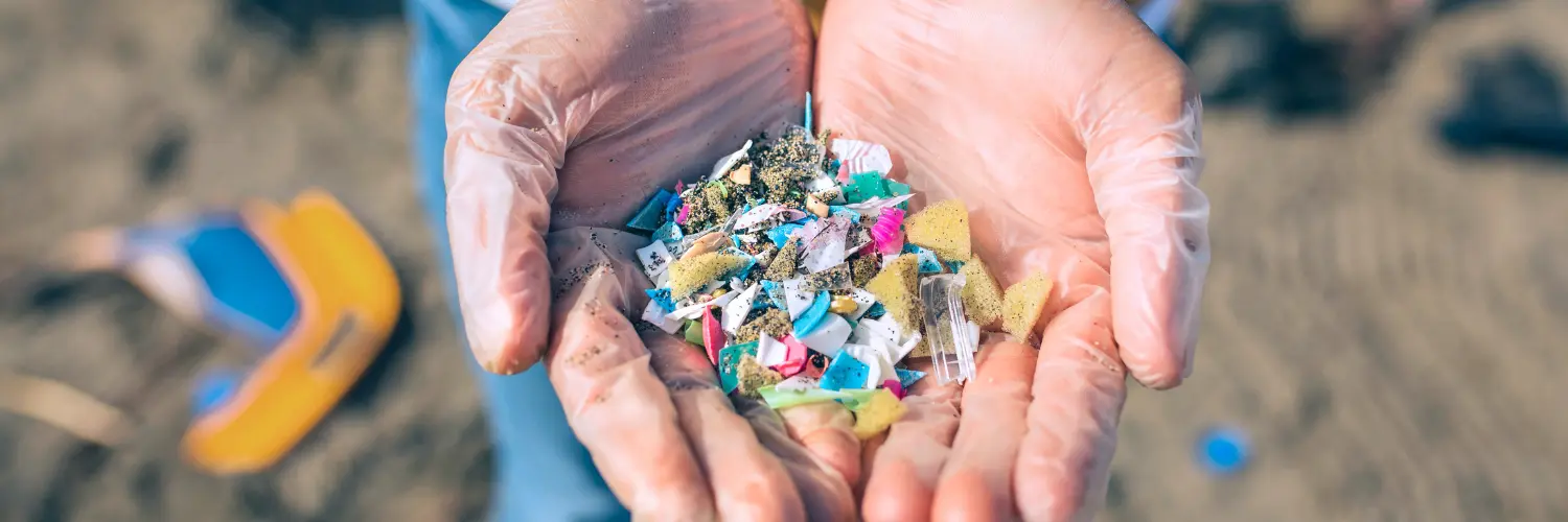 Hände mit Handschuhen bedeckt halten bunte Mikroplastikstückchen am Strand in der Hand