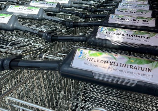 Rijen winkelwagentjes met 'Welkom bij Intratuin'-borden, opgesteld buiten een winkel onder een gestreepte luifel.