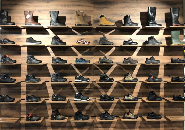 Wand in een schoenenwinkel met rijen herenschoenen en laarzen die op houten planken staan uitgestald.