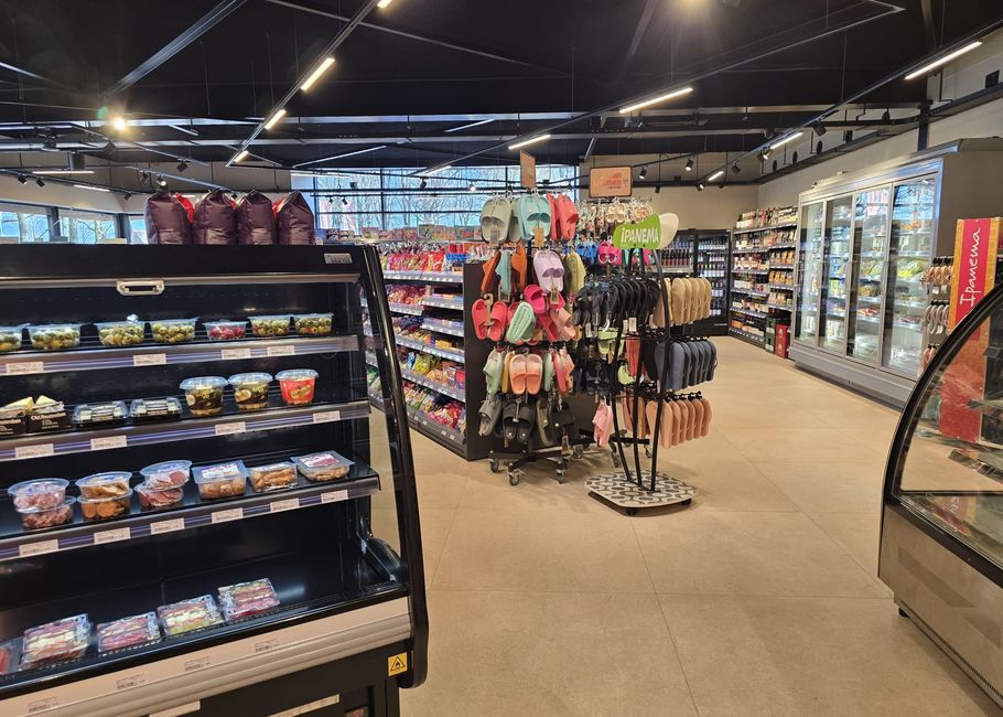 Een modern gangpad van een supermarkt met verpakt voedsel in de schappen, kleurrijke tassen en gekoelde afdelingen op de achtergrond.