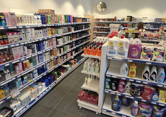 Een winkelpad met aan de linkerkant schappen gevuld met diverse producten voor persoonlijke verzorging en aan de rechterkant huishoudelijke schoonmaakmiddelen.
