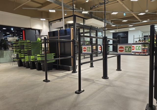 Lege winkelingang met zwarte slagbomen en bordjes met "geen toegang". Op de achtergrond zijn stapels groene manden en planken zichtbaar.