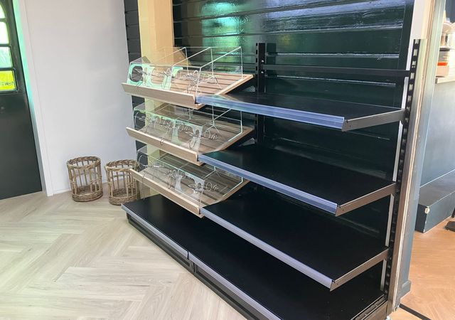 Lege zwarte winkelschappen met duidelijke scheidingslijnen in een winkel. Op de achtergrond zijn lichte houten vloeren en rieten manden zichtbaar.
