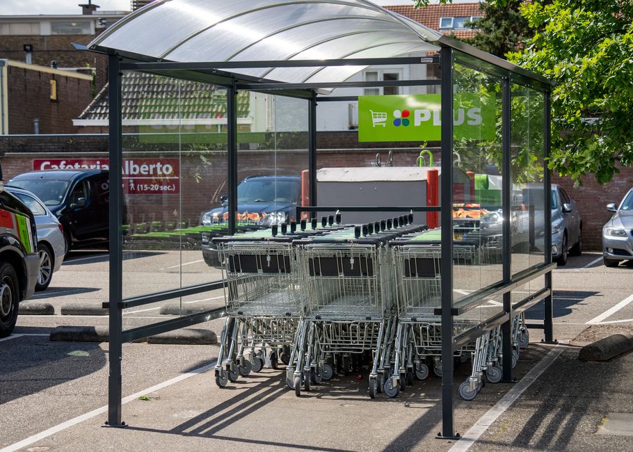 Winkelwagentjes staan ​​netjes gestapeld in een glazen en metalen karretje op een parkeerplaats, met een groen supermarktbord op de achtergrond.