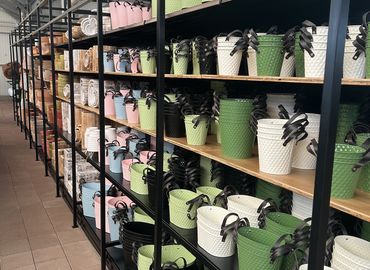 Rijen kleurrijke geweven manden in groen, roze en wit op metalen planken in een winkel.