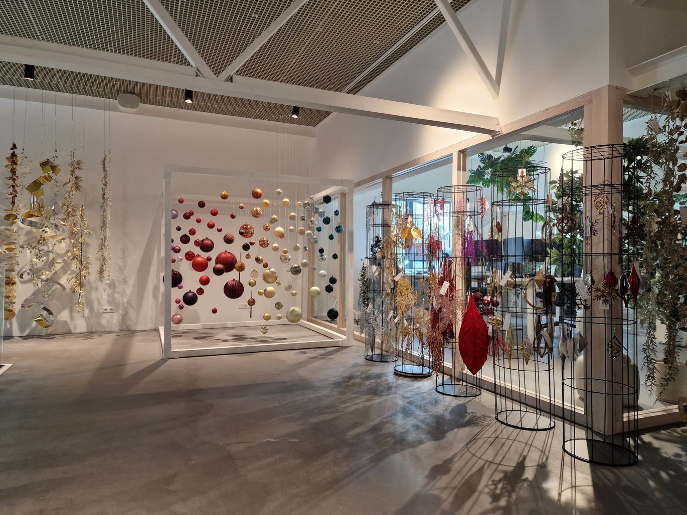 Een moderne kunstgalerie met hangende bolvormige sculpturen en kleurrijke decoraties op draadstandaards, gelegen in een ruime, goed verlichte kamer.