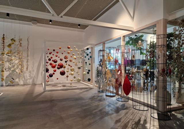 Een moderne kunstgalerie met hangende bolvormige sculpturen en kleurrijke decoraties op draadstandaards, gelegen in een ruime, goed verlichte kamer.