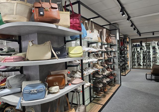 Licht boetiekpad met planken waarop diverse handtassen en schoenen worden uitgestald, handtassen op ronde planken links en rijen schoenen rechts.