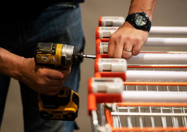 Persoon die een gele boormachine gebruikt om winkelwagentjes te repareren of in elkaar te zetten, met een horloge en ring, met de nadruk op handen en gereedschap.