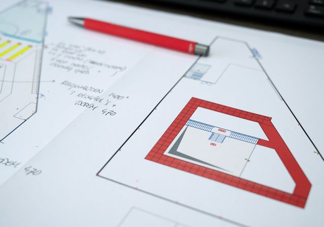 Architectuurplannen met rode pen op een bureau, met gedetailleerde vloerindelingen en handgeschreven notities.