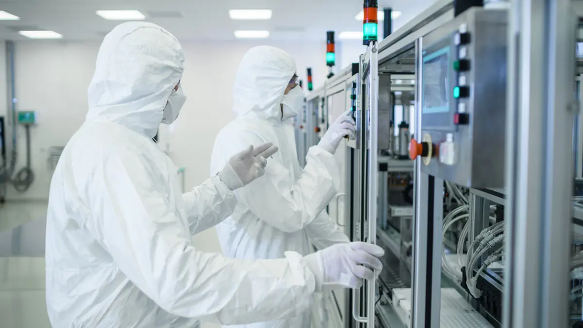 Workers are setting up machines in front of equipment in a sterile room.