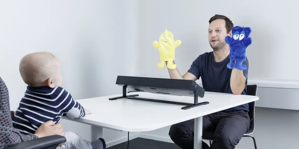 An infant in front of Tobii Pro Spectrum eye tracker looks at a researcher with poppets 