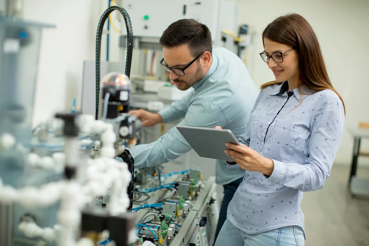 Two workers are setting up electronic component manufacturing equipment.