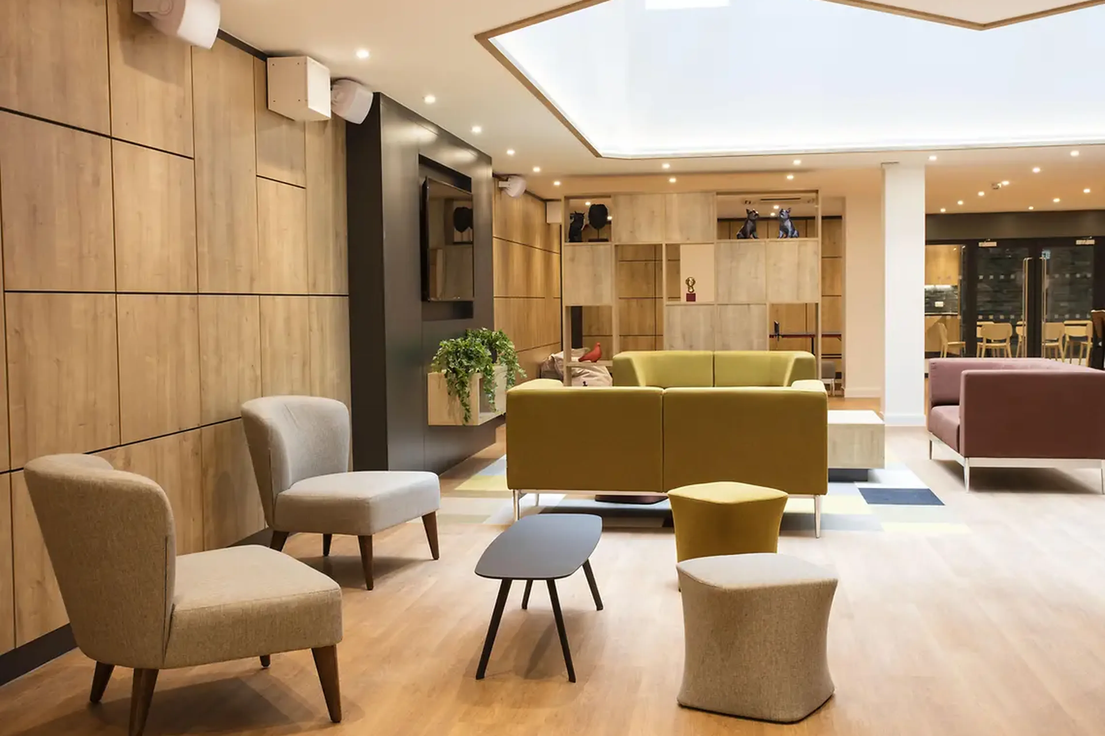 Modern lounge with wooden walls, assorted chairs, a green sofa, and skylight, creating a cozy and inviting atmosphere.