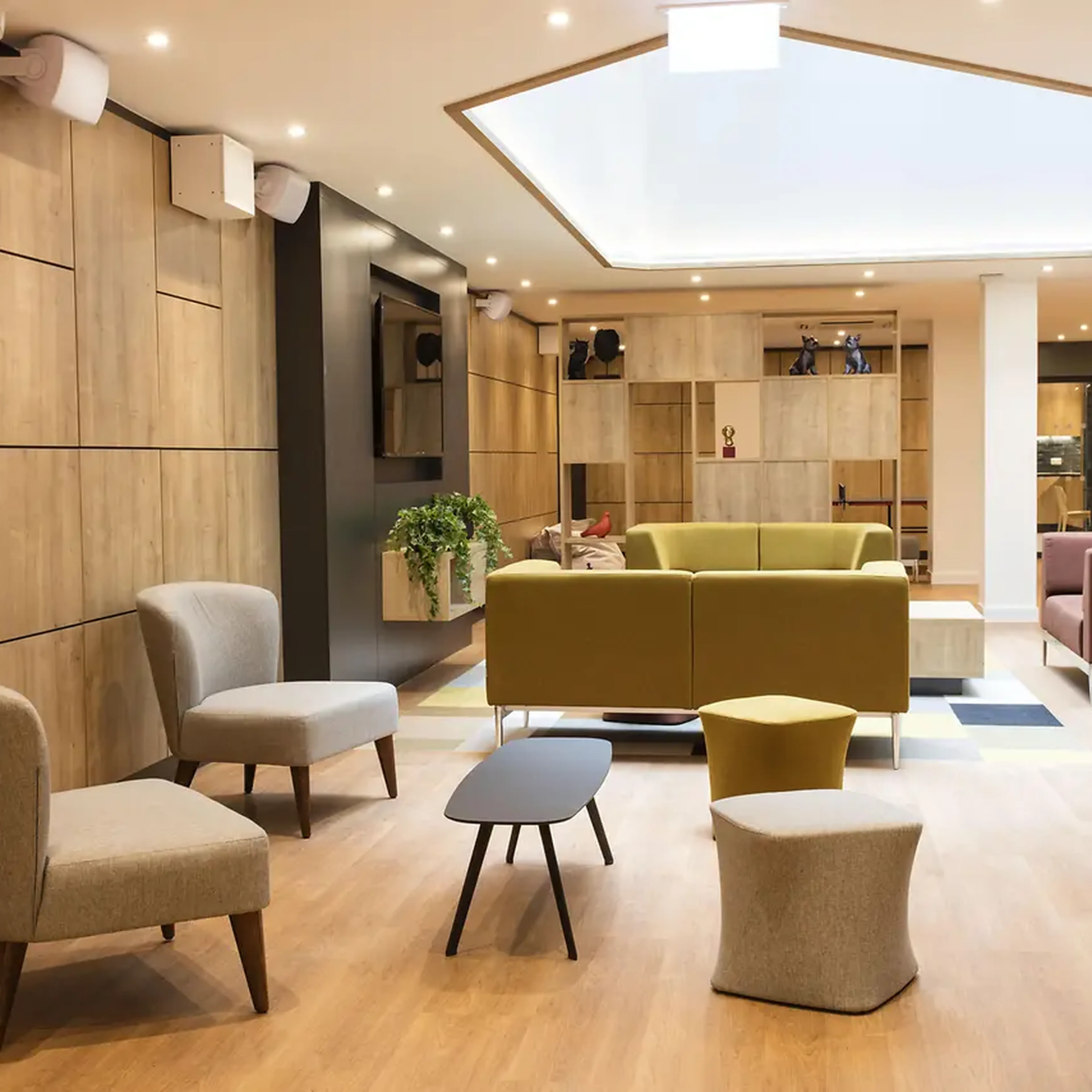 Modern lounge with wooden walls, assorted chairs, a green sofa, and skylight, creating a cozy and inviting atmosphere.