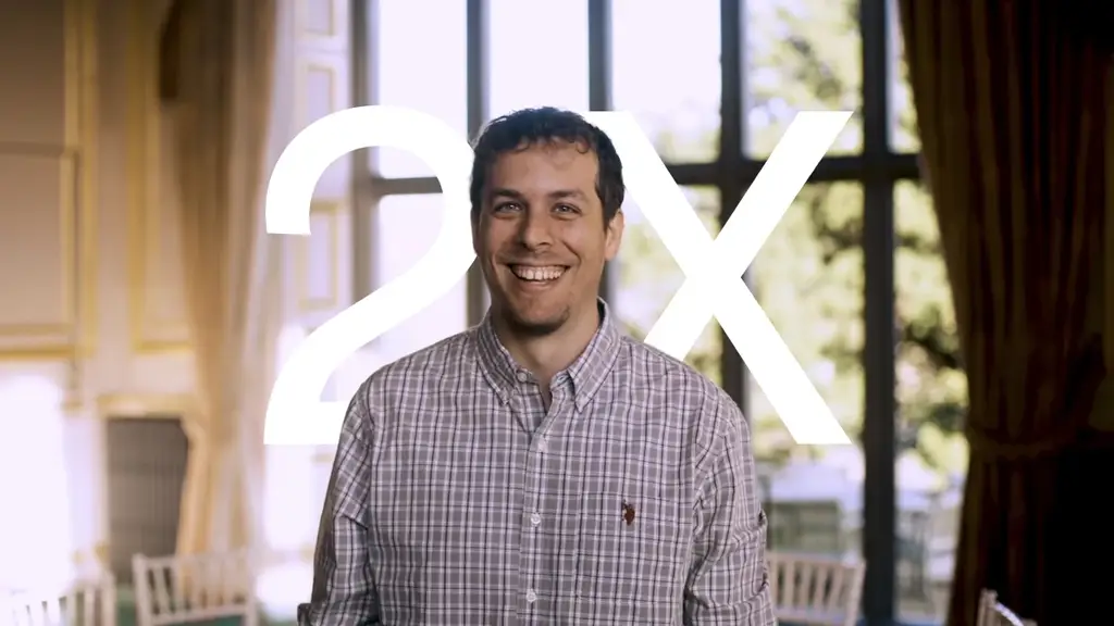 Smiling man in checked shirt stands in front of large "2X" text overlay.