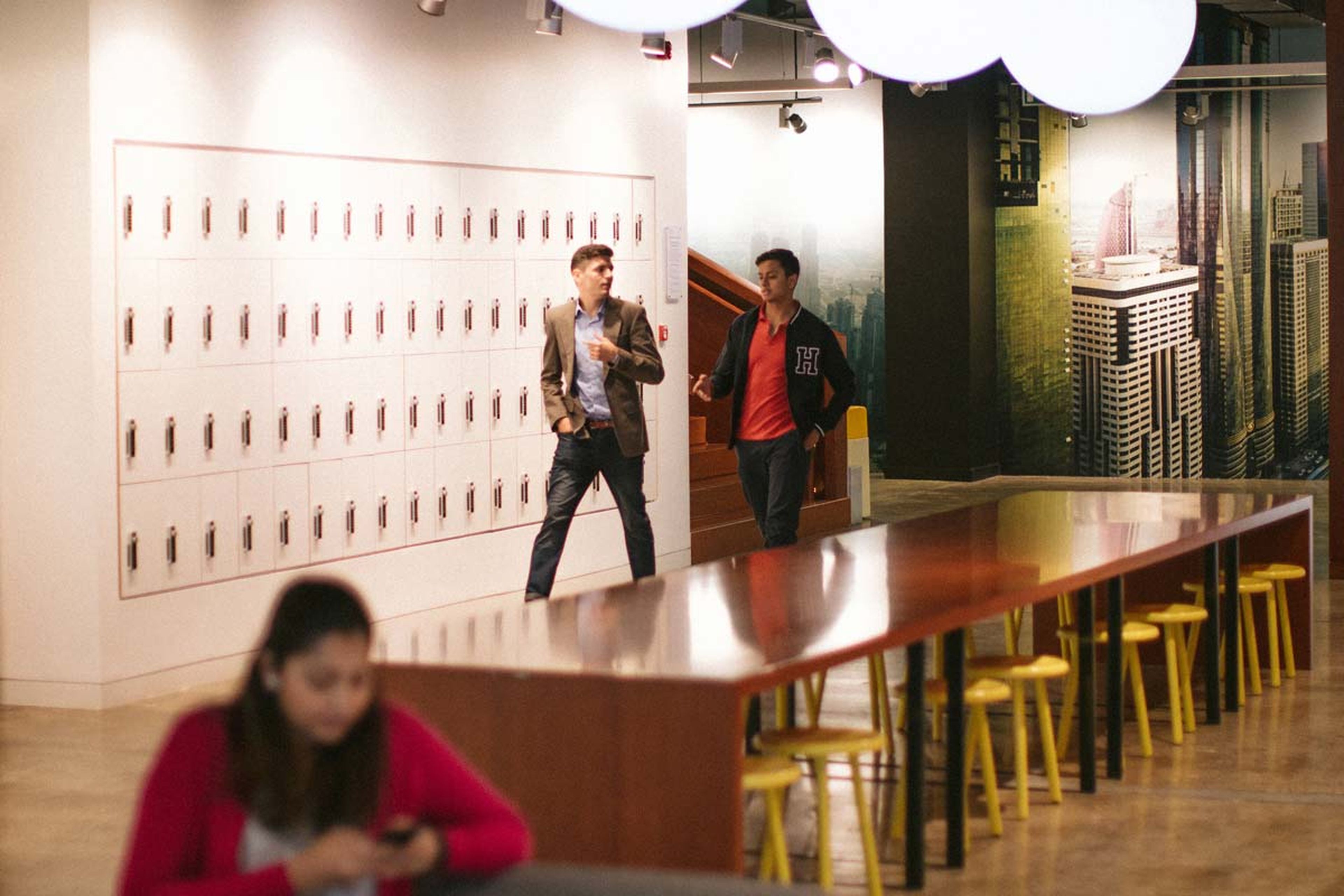 Two People walking in a modern office space hallway and a woman is using her phone.