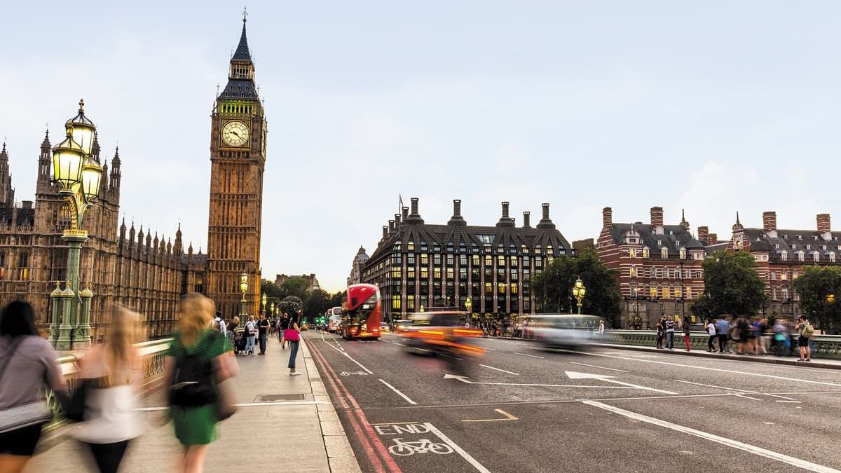 People walking on a bridge near Big Ben in London, with blurred traffic passing by.