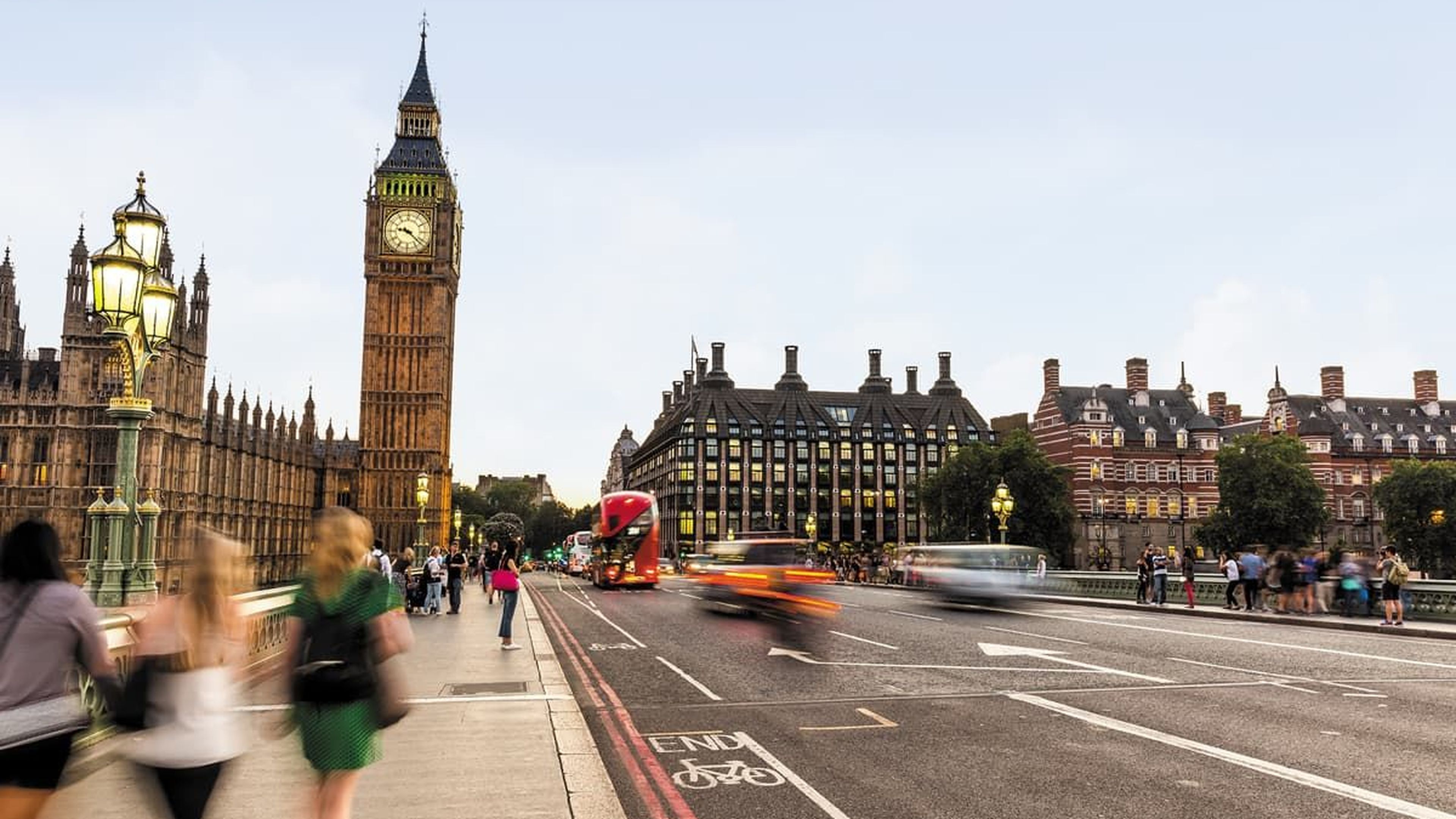 People walking on a bridge near Big Ben in London, with blurred traffic passing by.