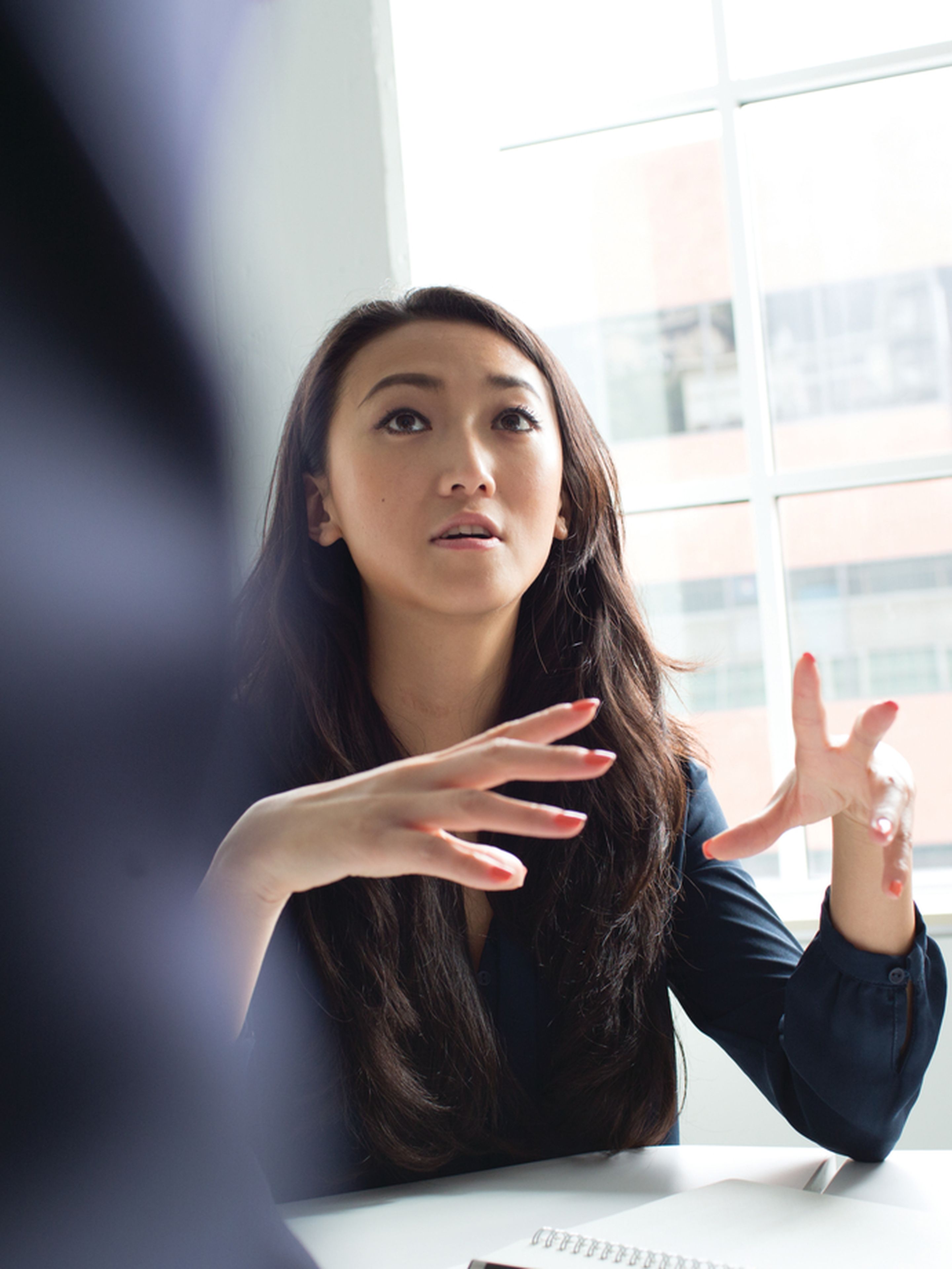 A woman gestures while speaking in a brightly lit office meeting.