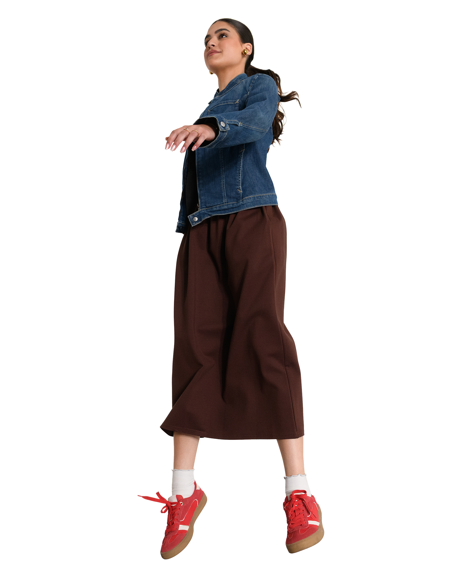 A woman in a denim jacket and brown pants appears to be floating, wearing red sneakers and white socks.