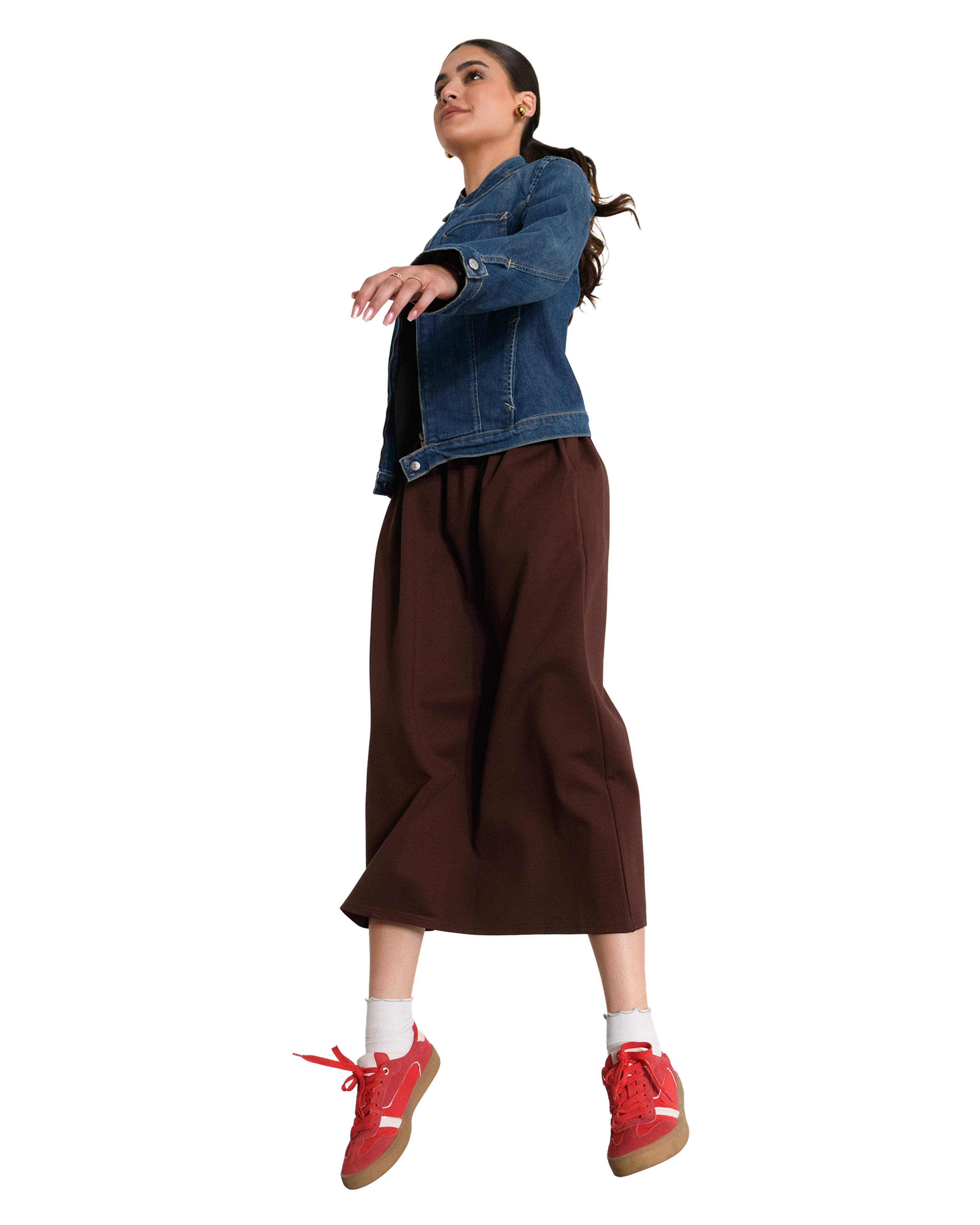 A woman in a denim jacket and brown pants appears to be floating, wearing red sneakers and white socks.