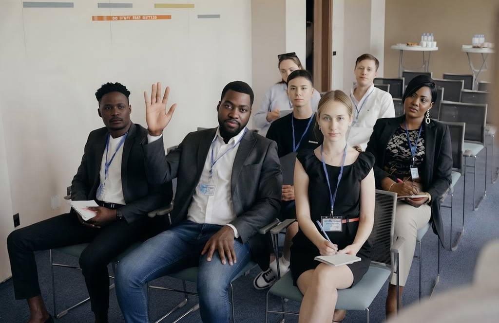 Diverse group of people sitting in a conference room, with one man raising his hand.