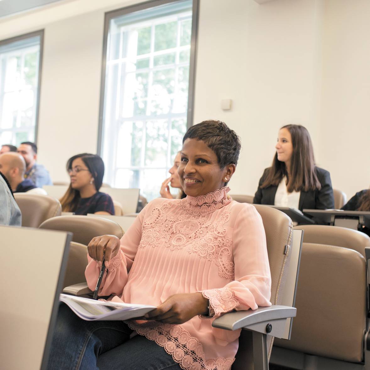 People sitting in a classroom, listening and smiling during a lecture.