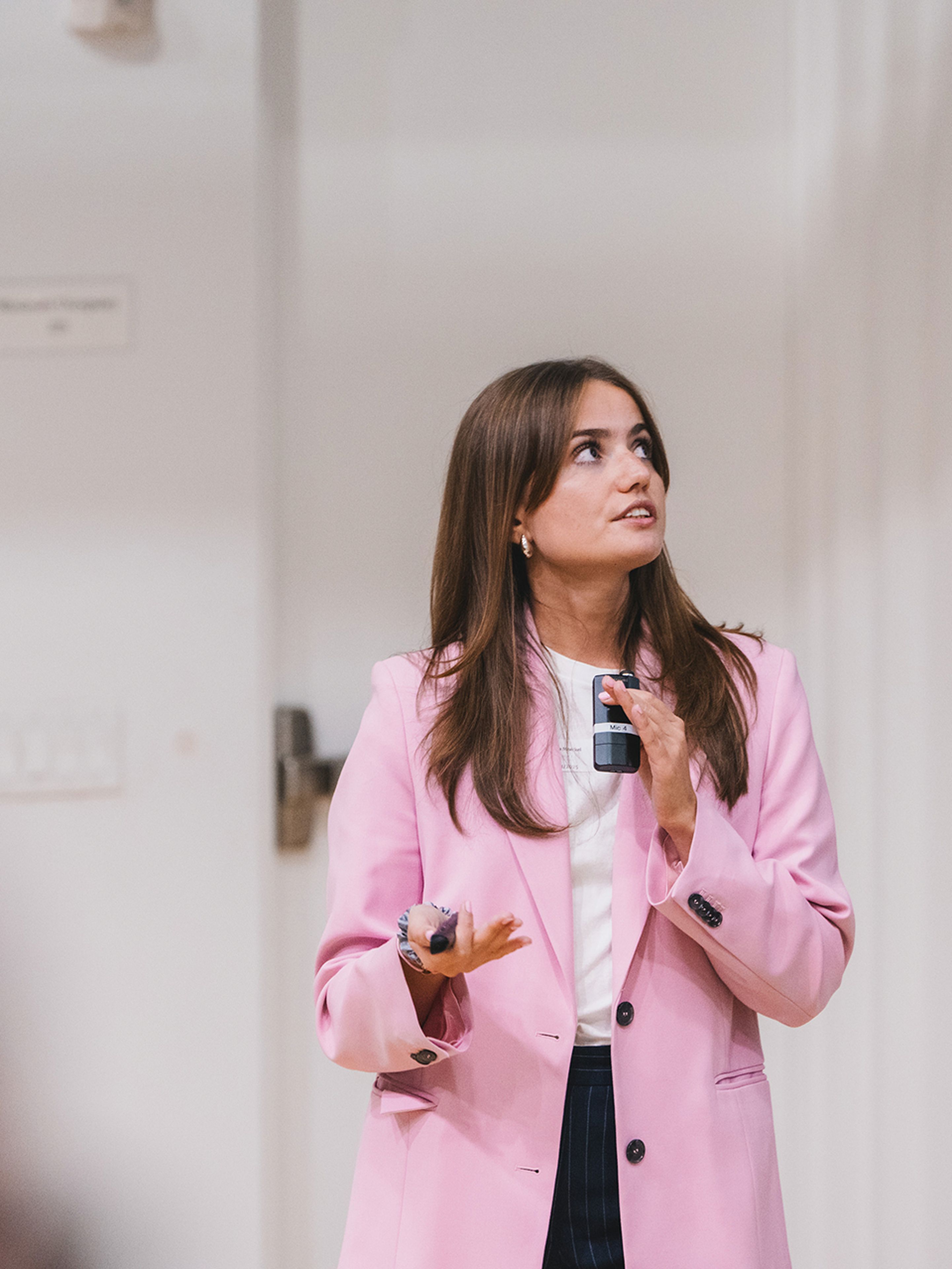 Woman in pink blazer giving a presentation, holding a clicker and looking attentively.