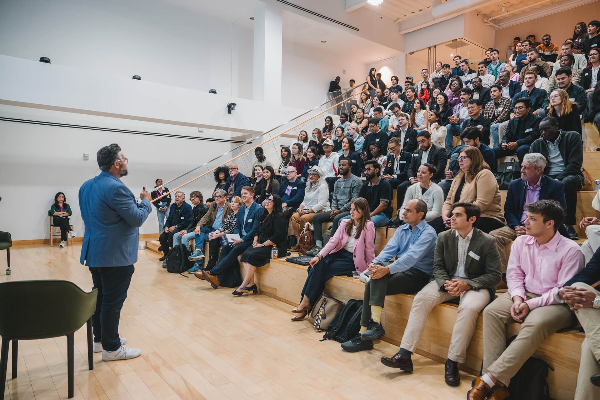A speaker addresses a large seated audience in a modern auditorium.