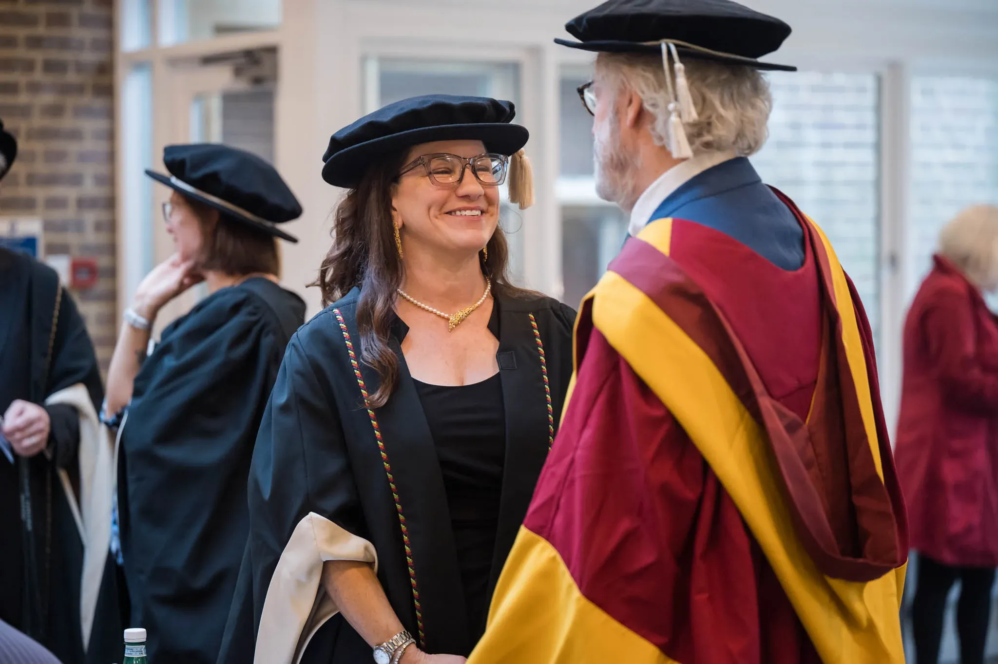 Two people in academic robes conversing and smiling during a graduation ceremony.