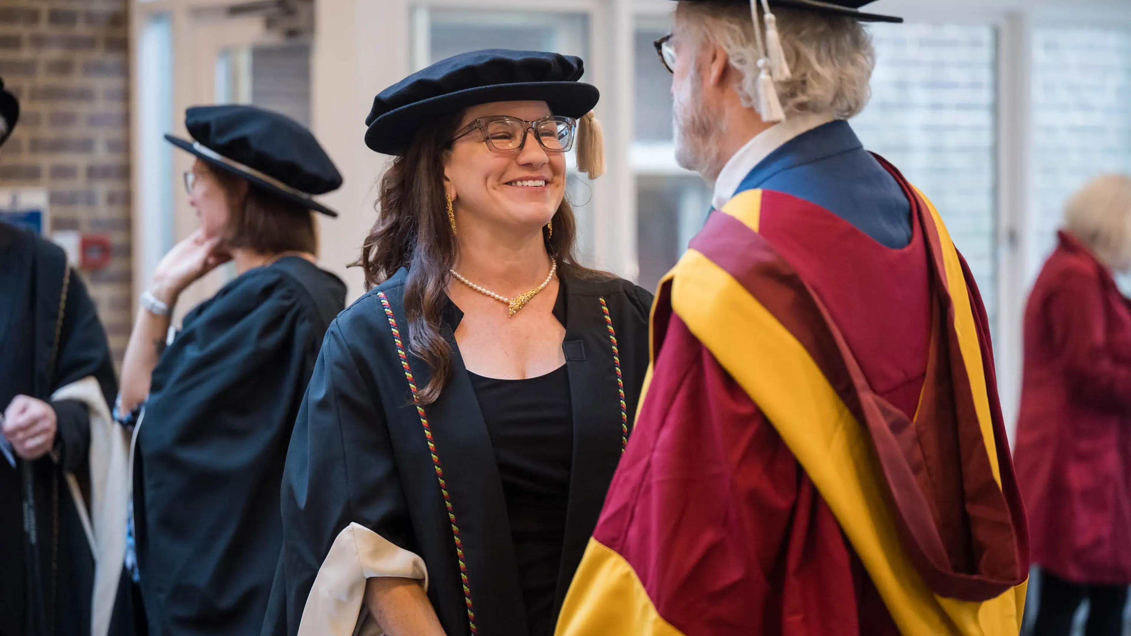Two people in academic robes conversing and smiling during a graduation ceremony.