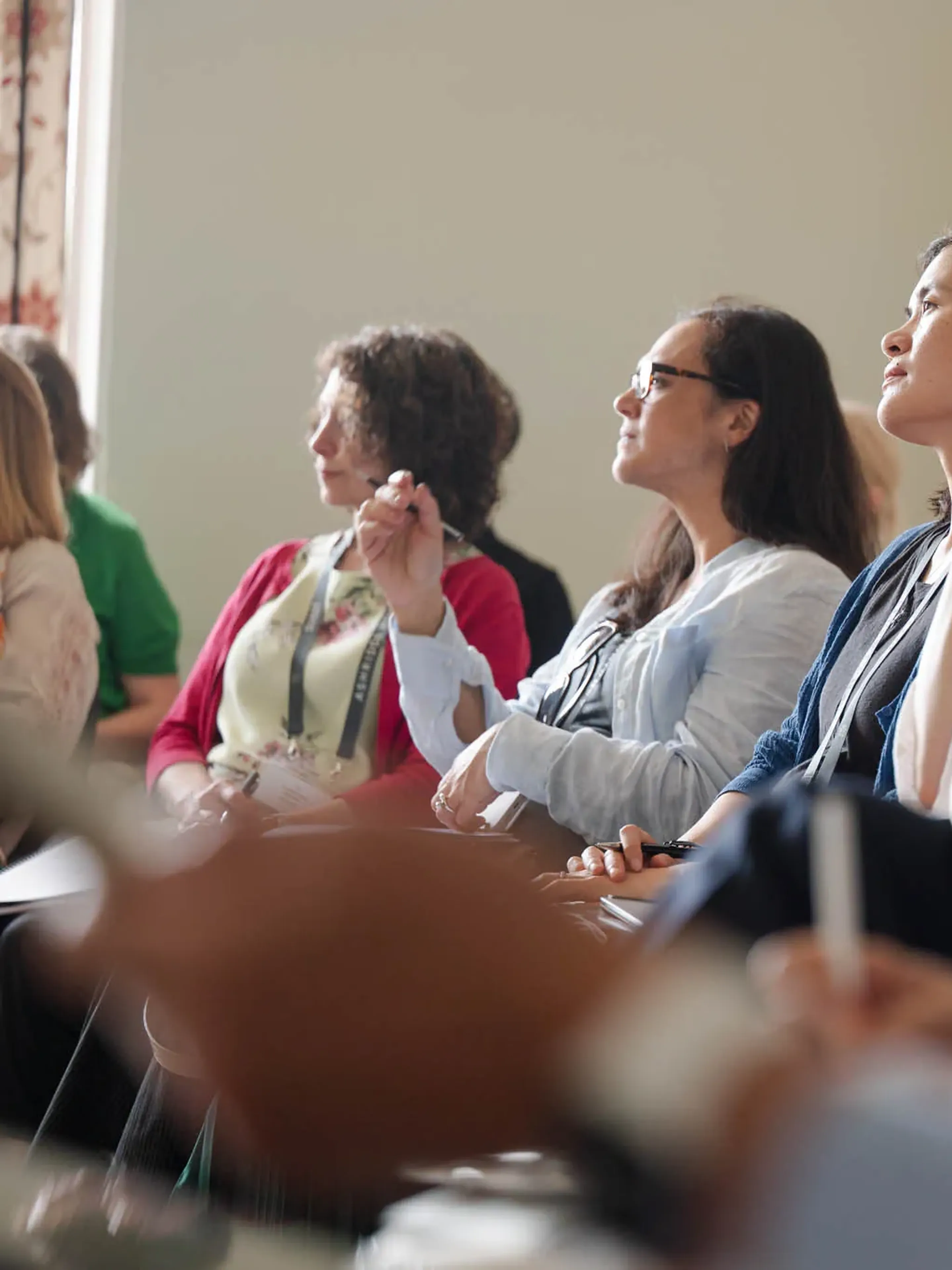 A diverse group of people attentively listens during a seminar, some taking notes.