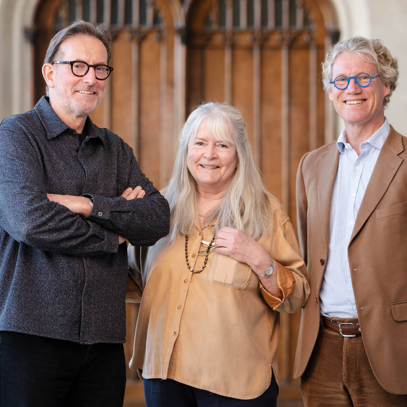 Three people smiling, standing together in front of wooden doors.