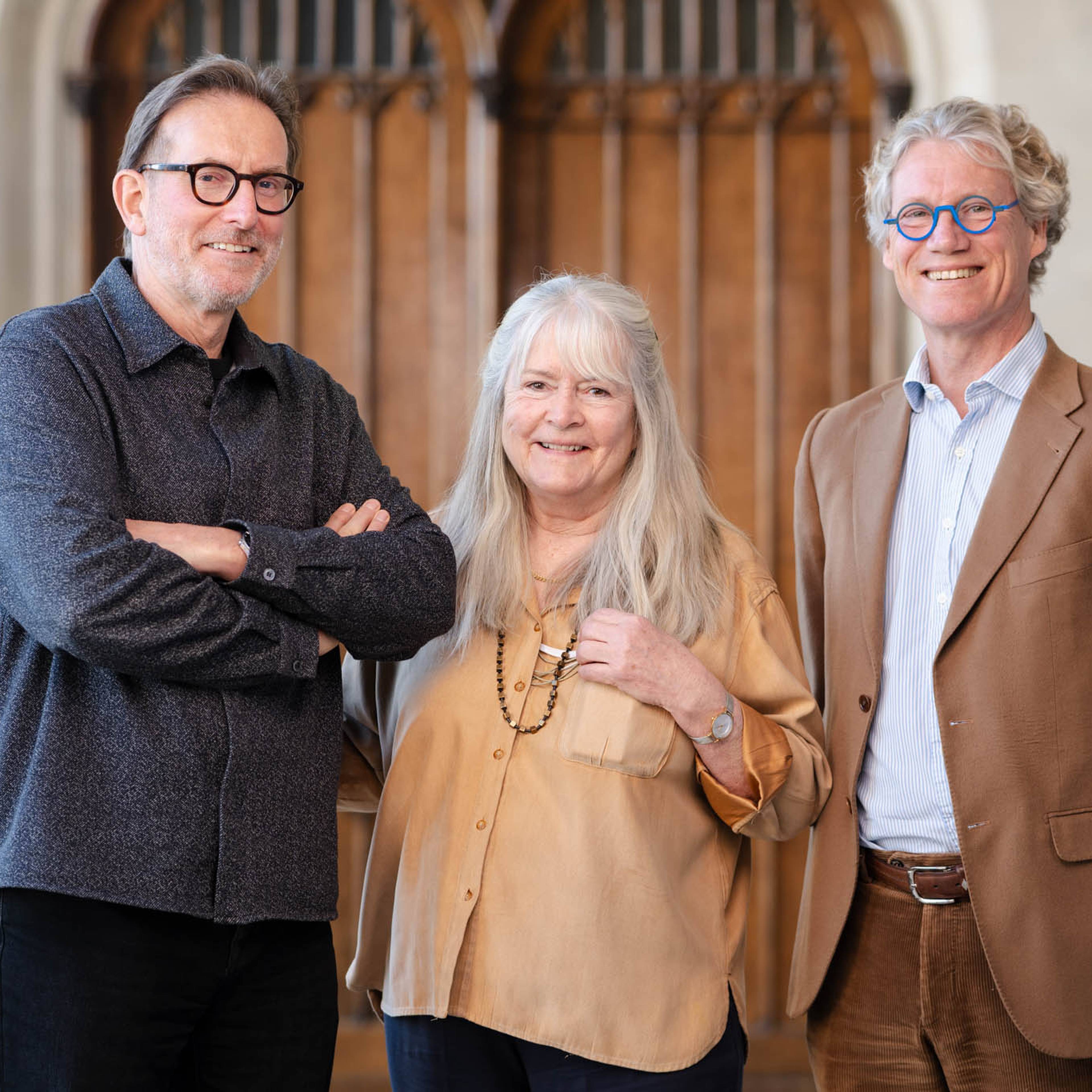 Three people smiling, standing together in front of wooden doors.