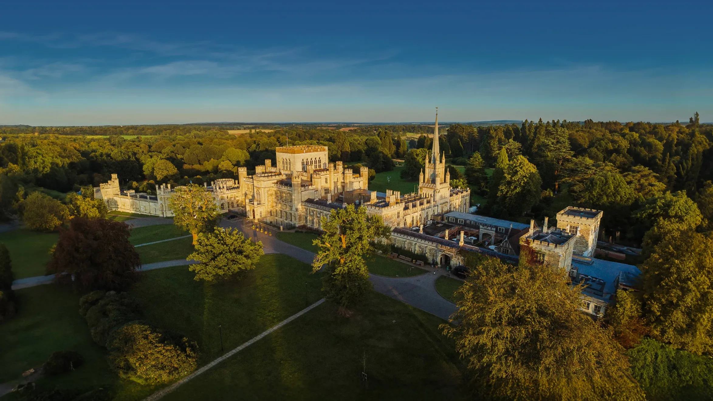 Aerial view of an expansive castle surrounded by lush green forests under a clear blue sky.