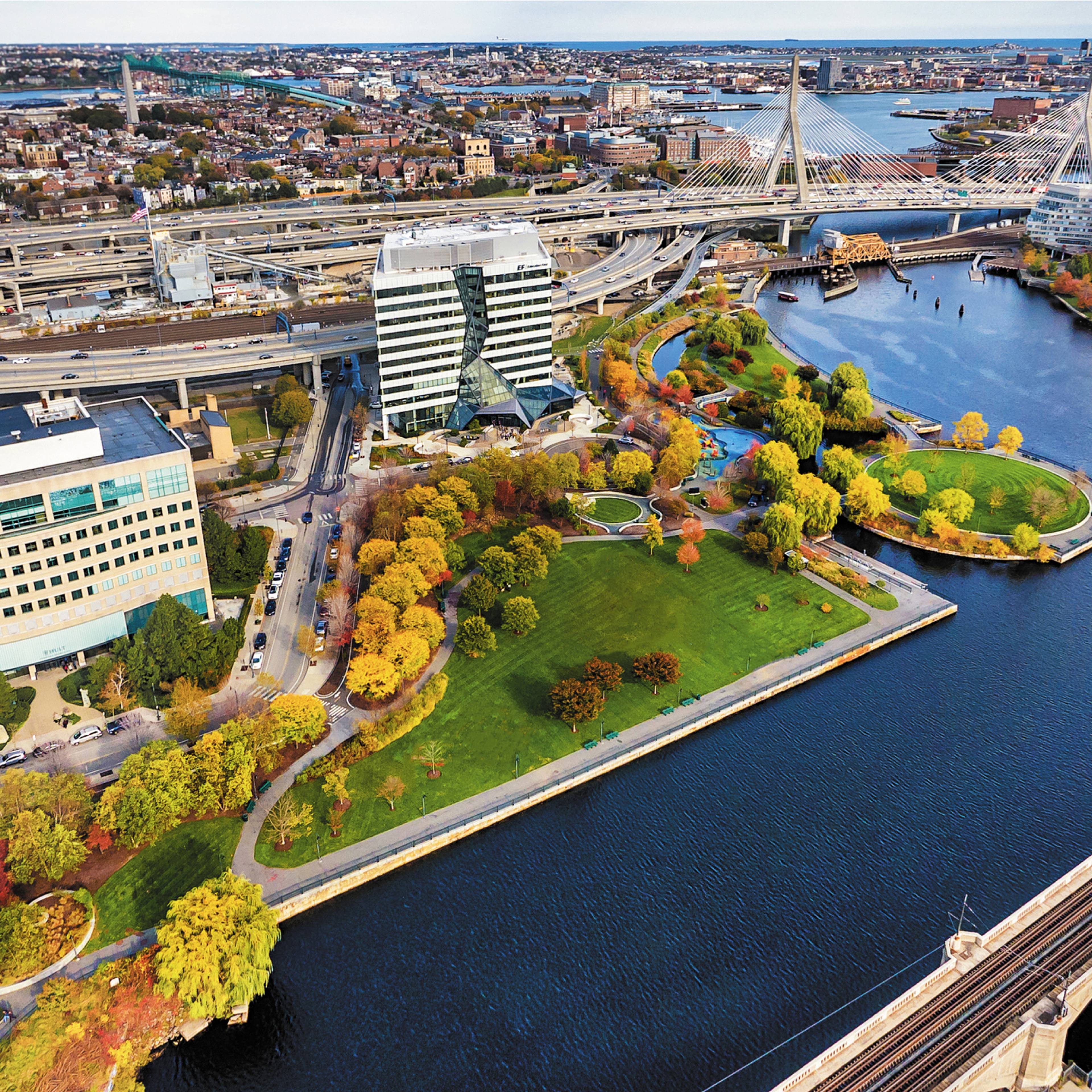 Aerial view of urban parkland surrounded by a river, roads, and buildings.