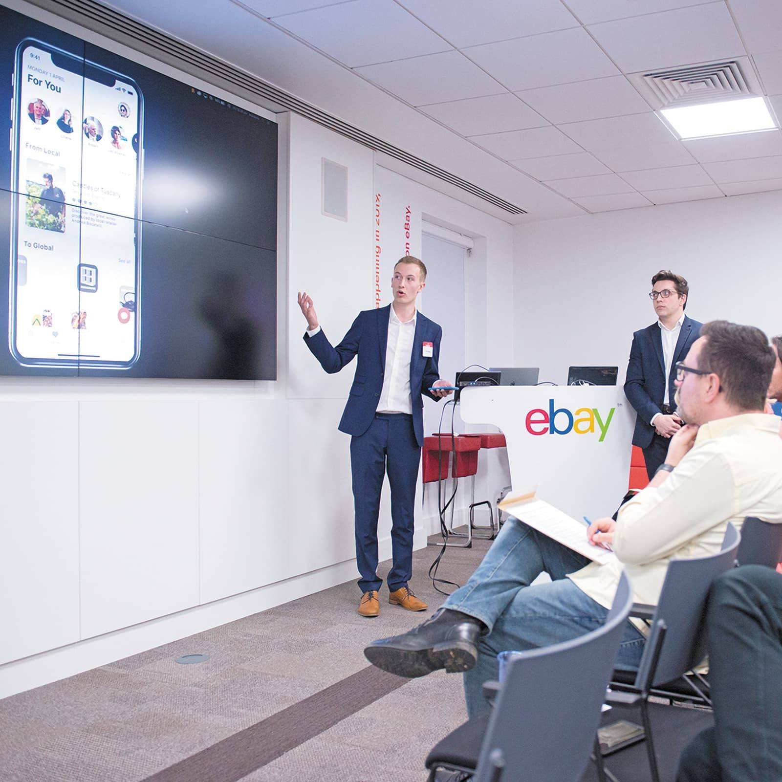 Two men present to an audience in a conference room with eBay logos.
