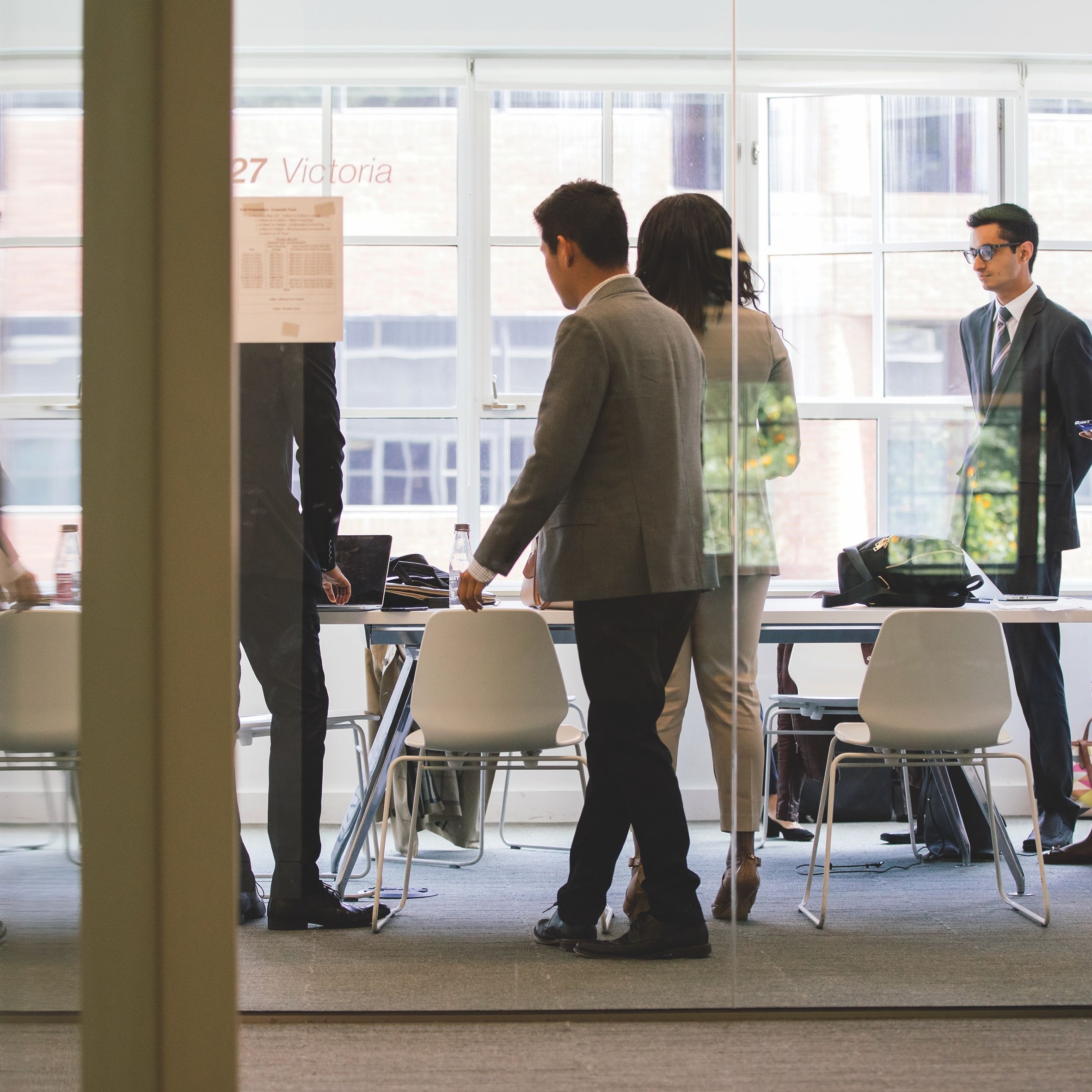 People in business attire having a meeting in a glass-walled office room.