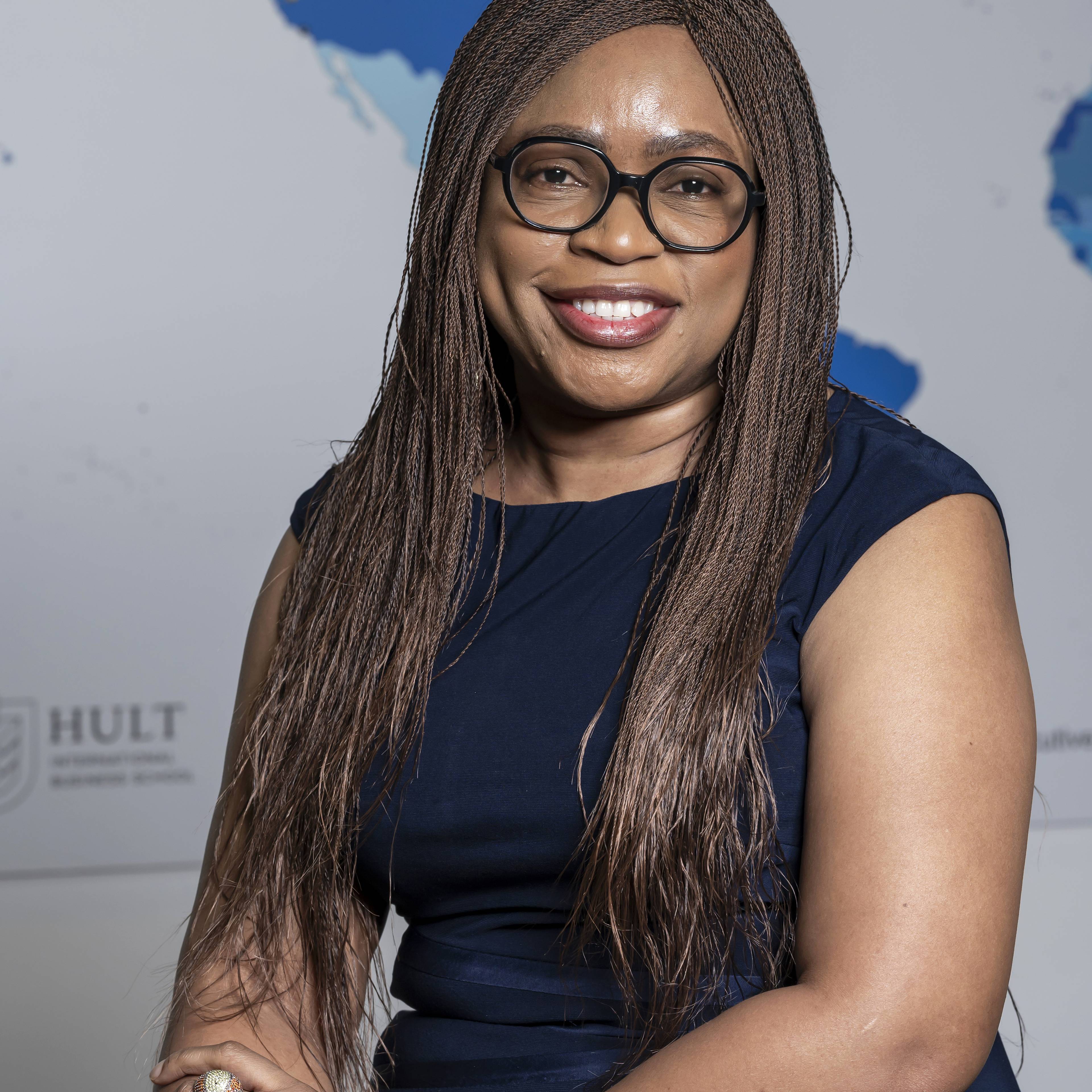 Smiling woman with glasses and braided hair poses in front of a world map.