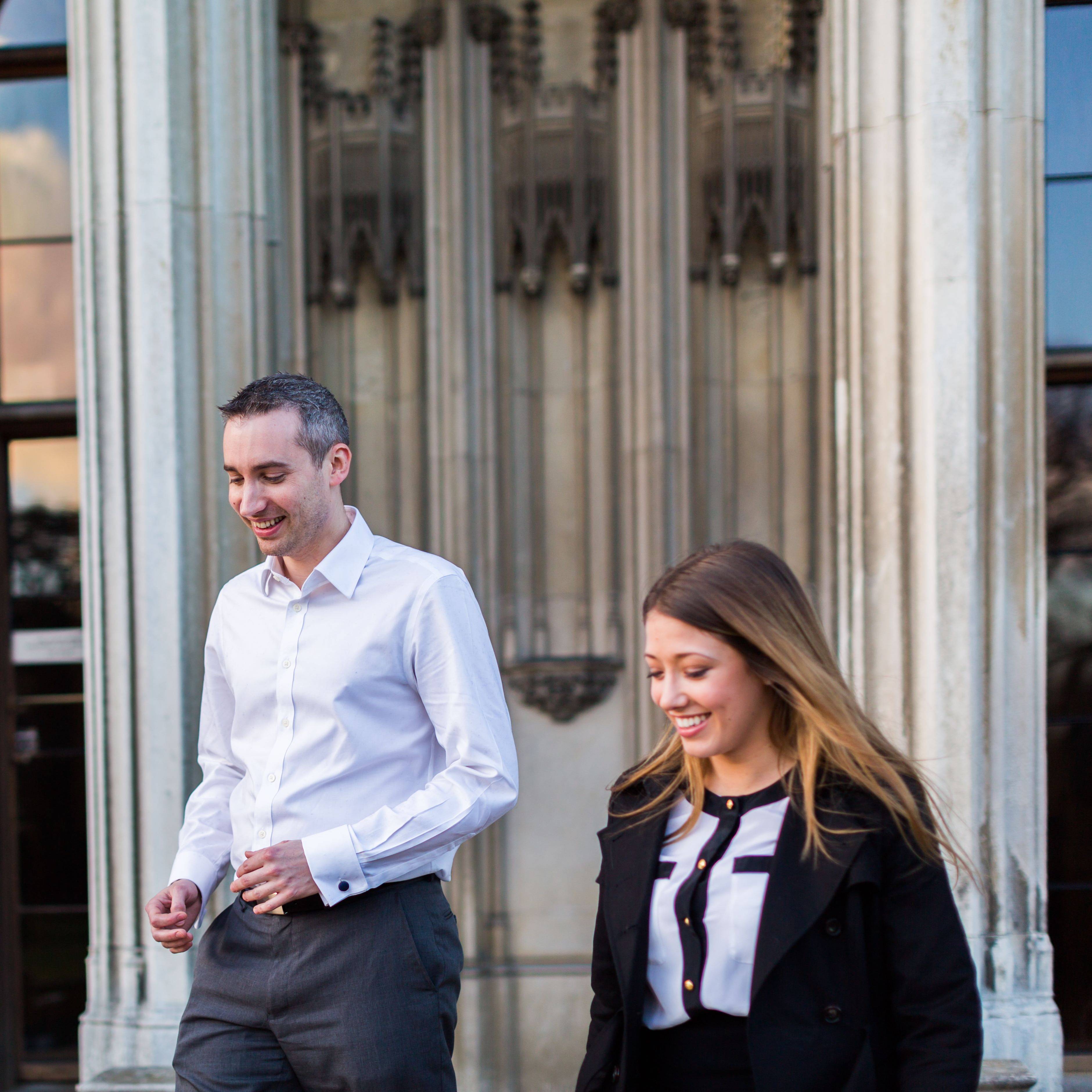 Two people walking and smiling in front of a large, ornate building entrance.