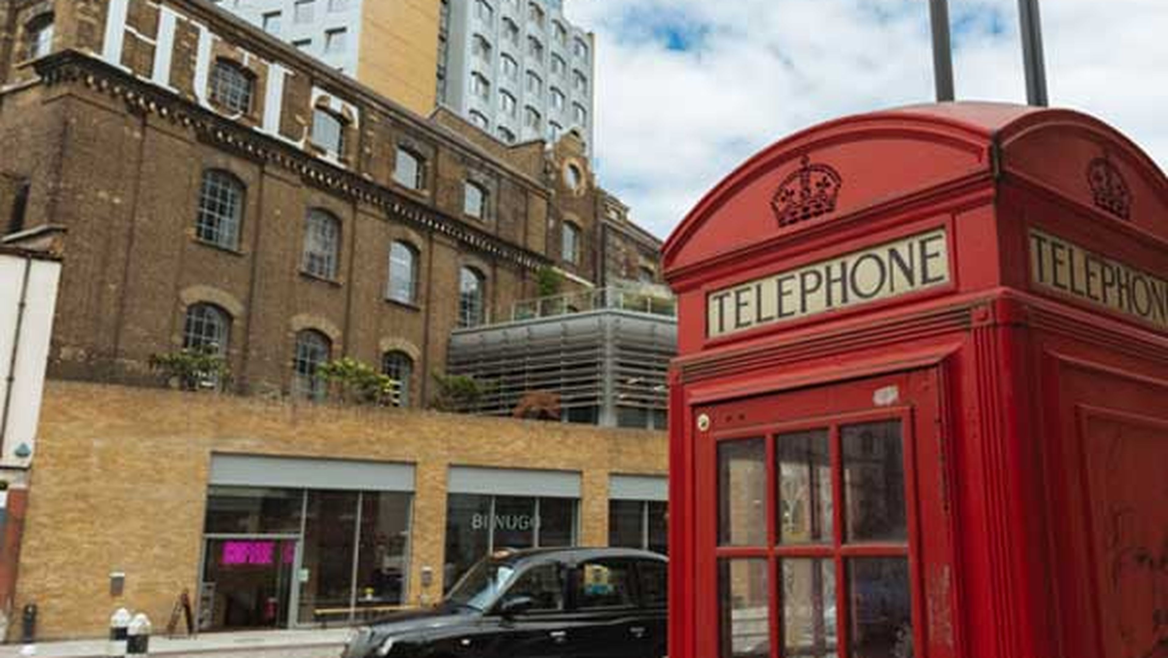 Red telephone booth beside a busy street with a taxi and historic building.
