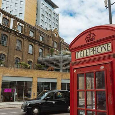 Red telephone booth beside a busy street with a taxi and historic building.