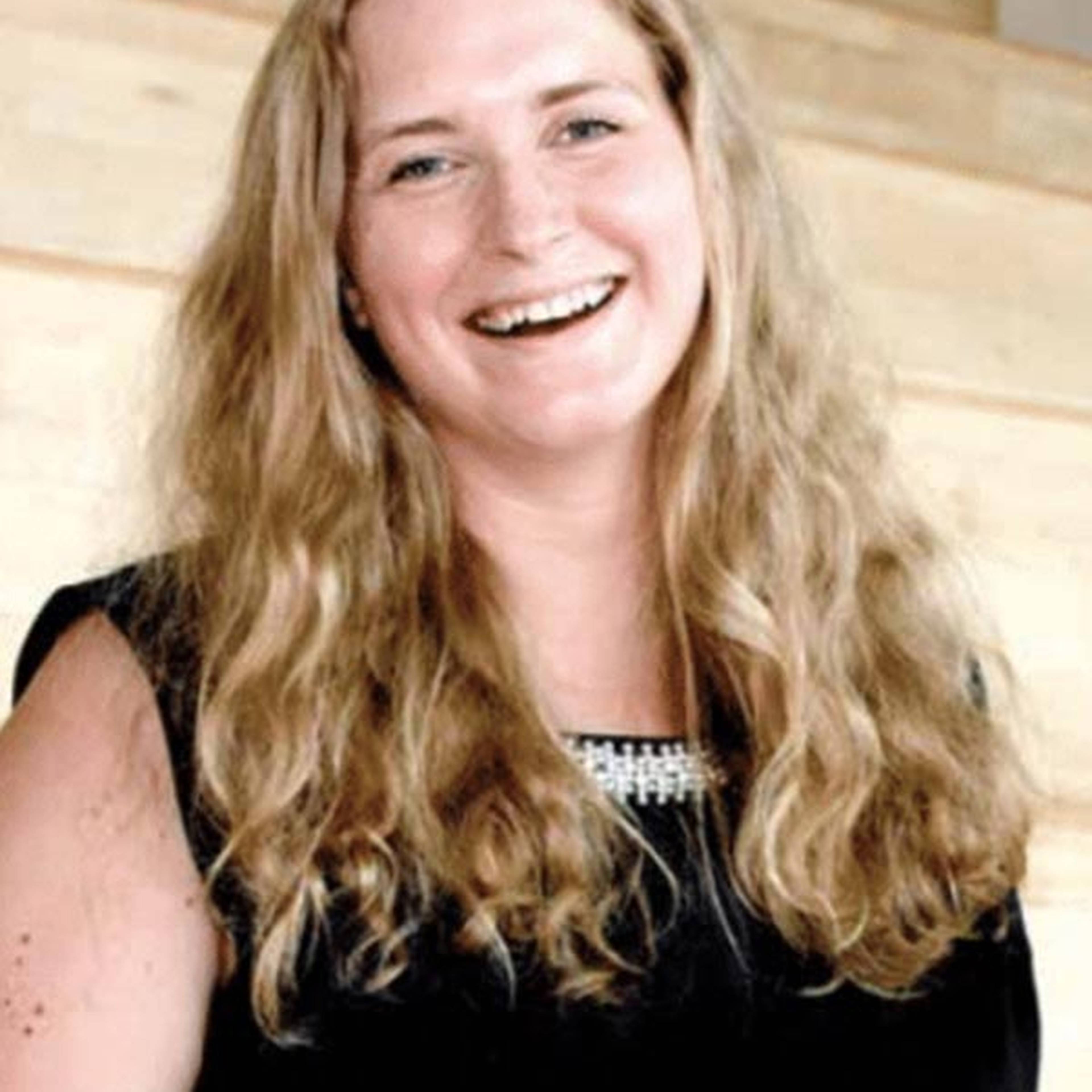 A woman smiling  in a setting with light wood paneling.