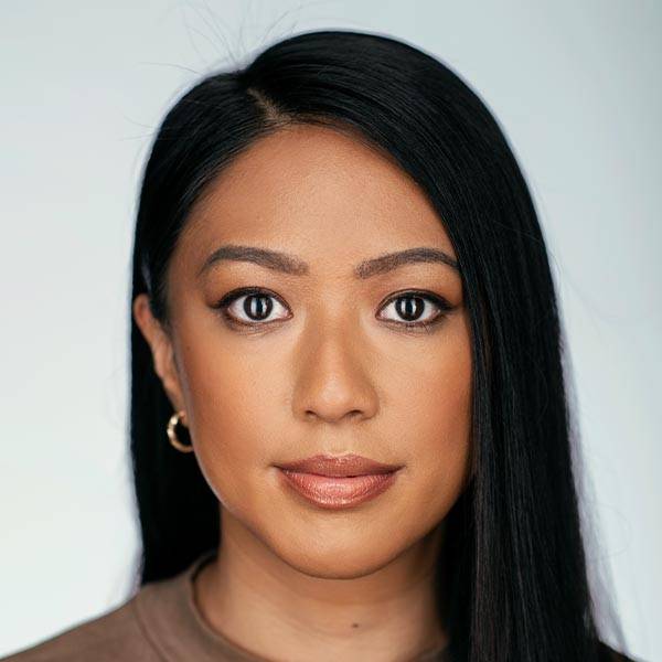 A woman with long black hair and hoop earrings looks directly at the camera.