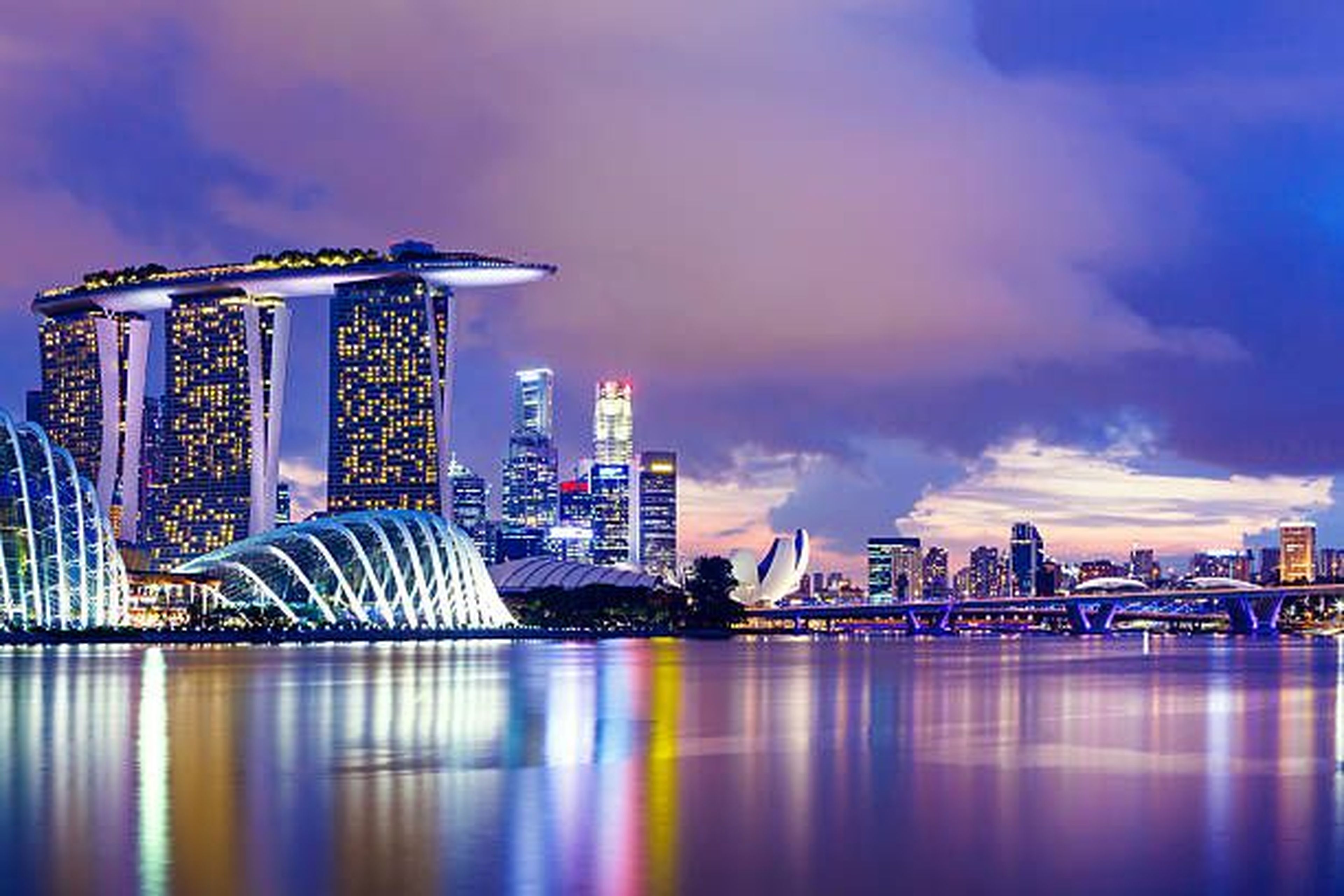 Singapore skyline at dusk with Marina Bay Sands and vibrant city lights reflecting on water.