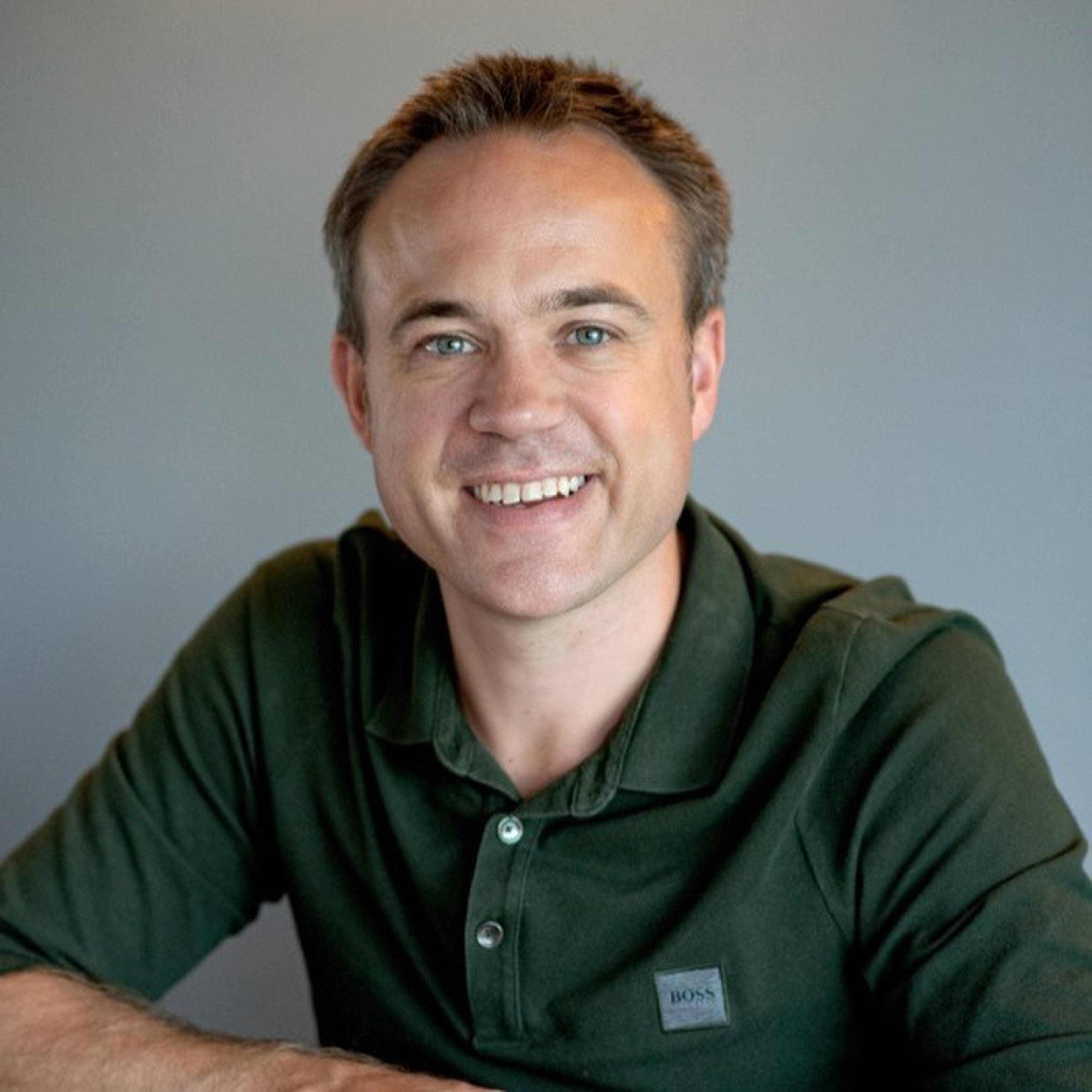 Smiling man in a green polo shirt against a gray background.