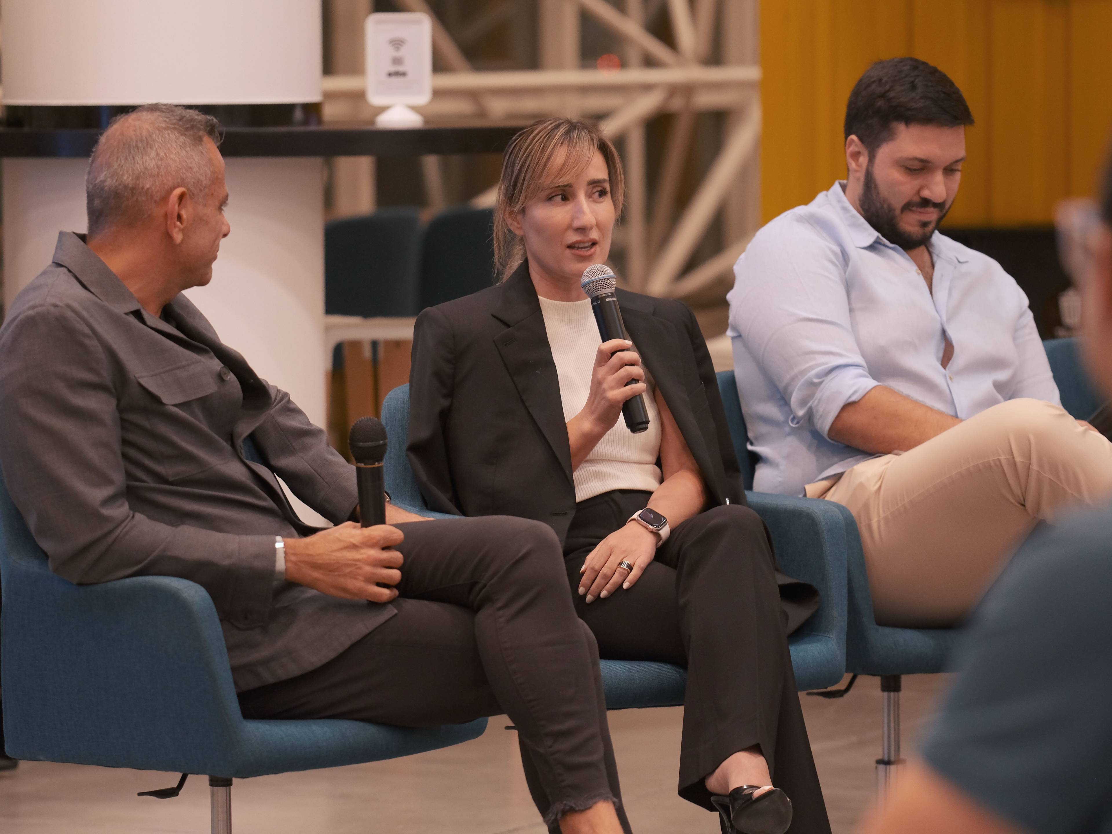 Three people seated, one woman speaking into a microphone during  UAE career event